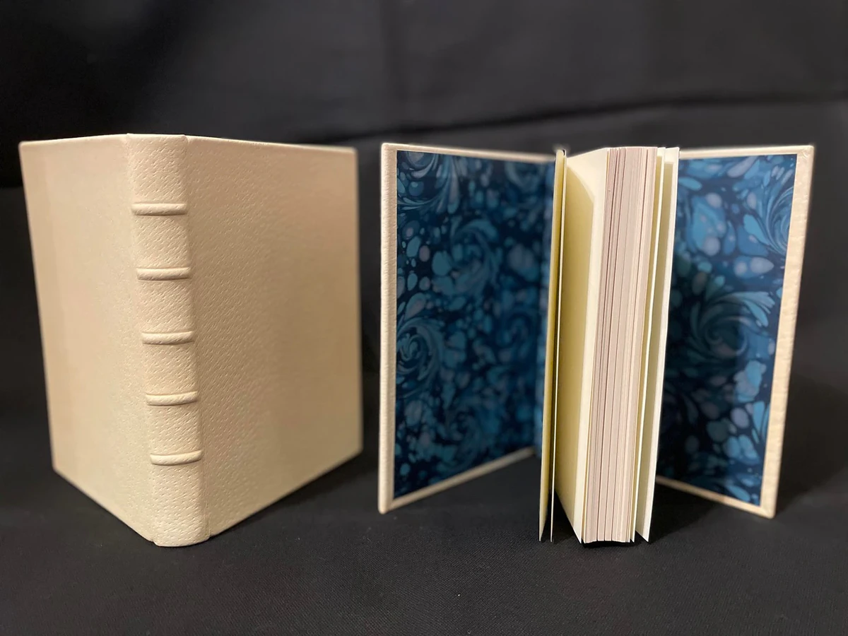 A Claimed binding prototype with raised bands beside an open copy with blue marbled placeholder endpapers